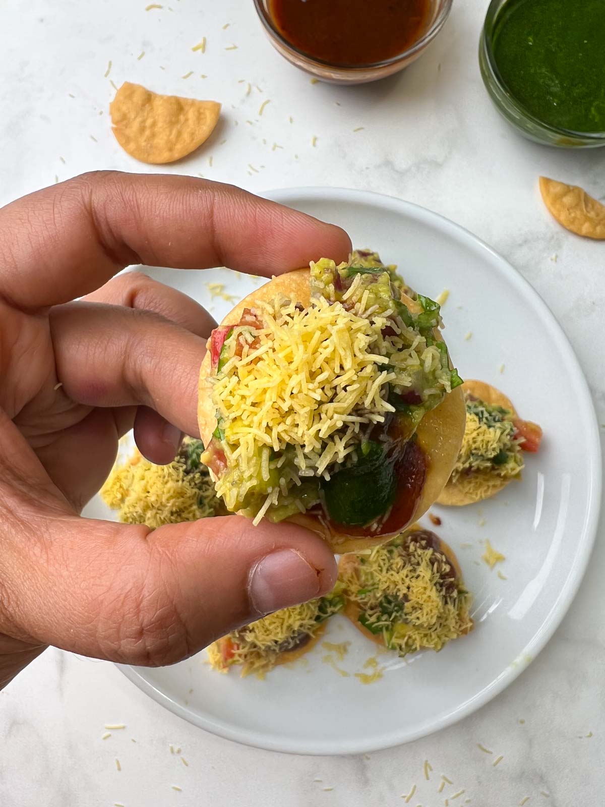 avocado papri chaat in a hand with chutneys on the side