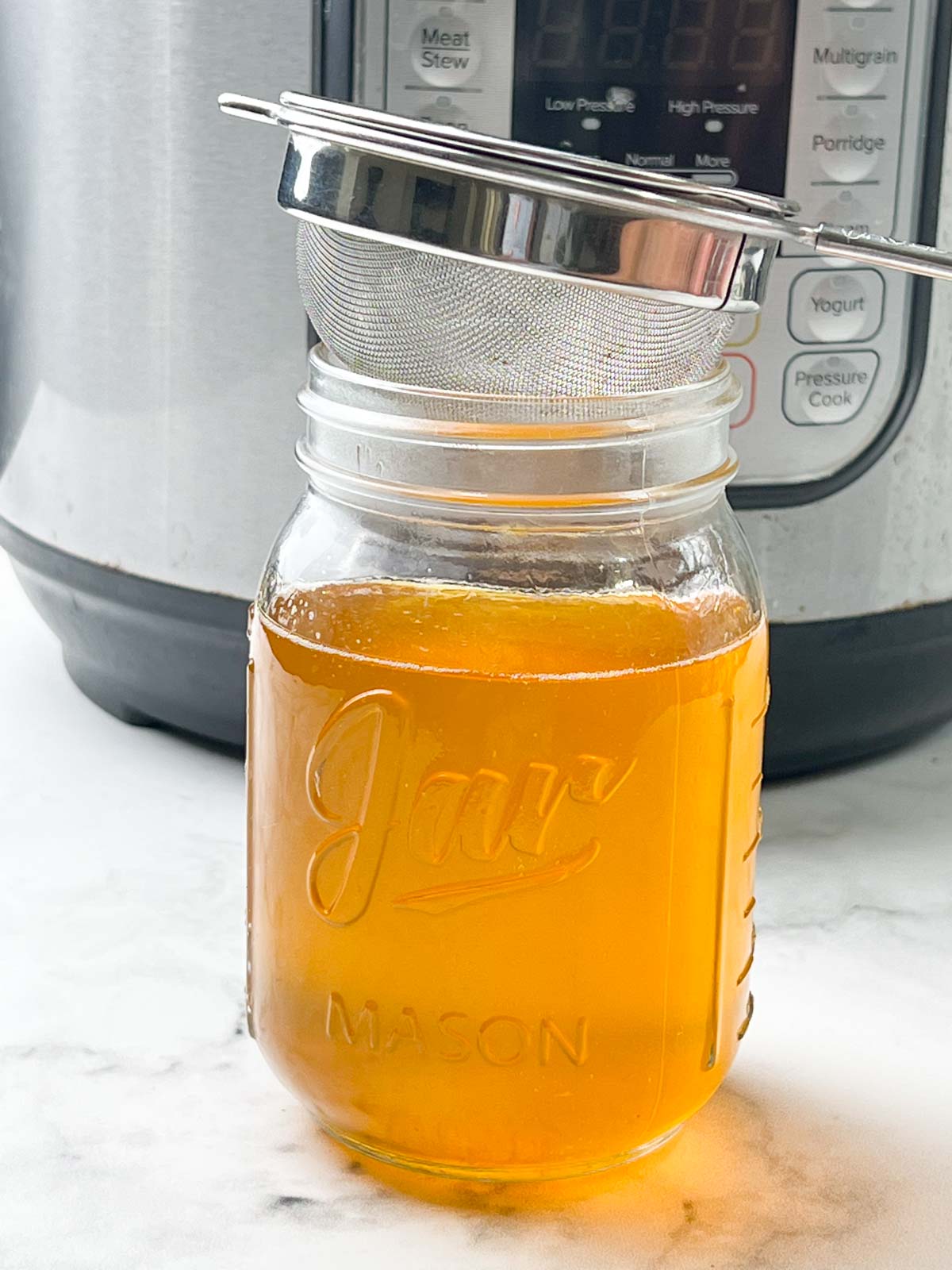 liquid gold aka ghee in a mason jar with fine mesh sieve on the glass jar with instant pot on the side