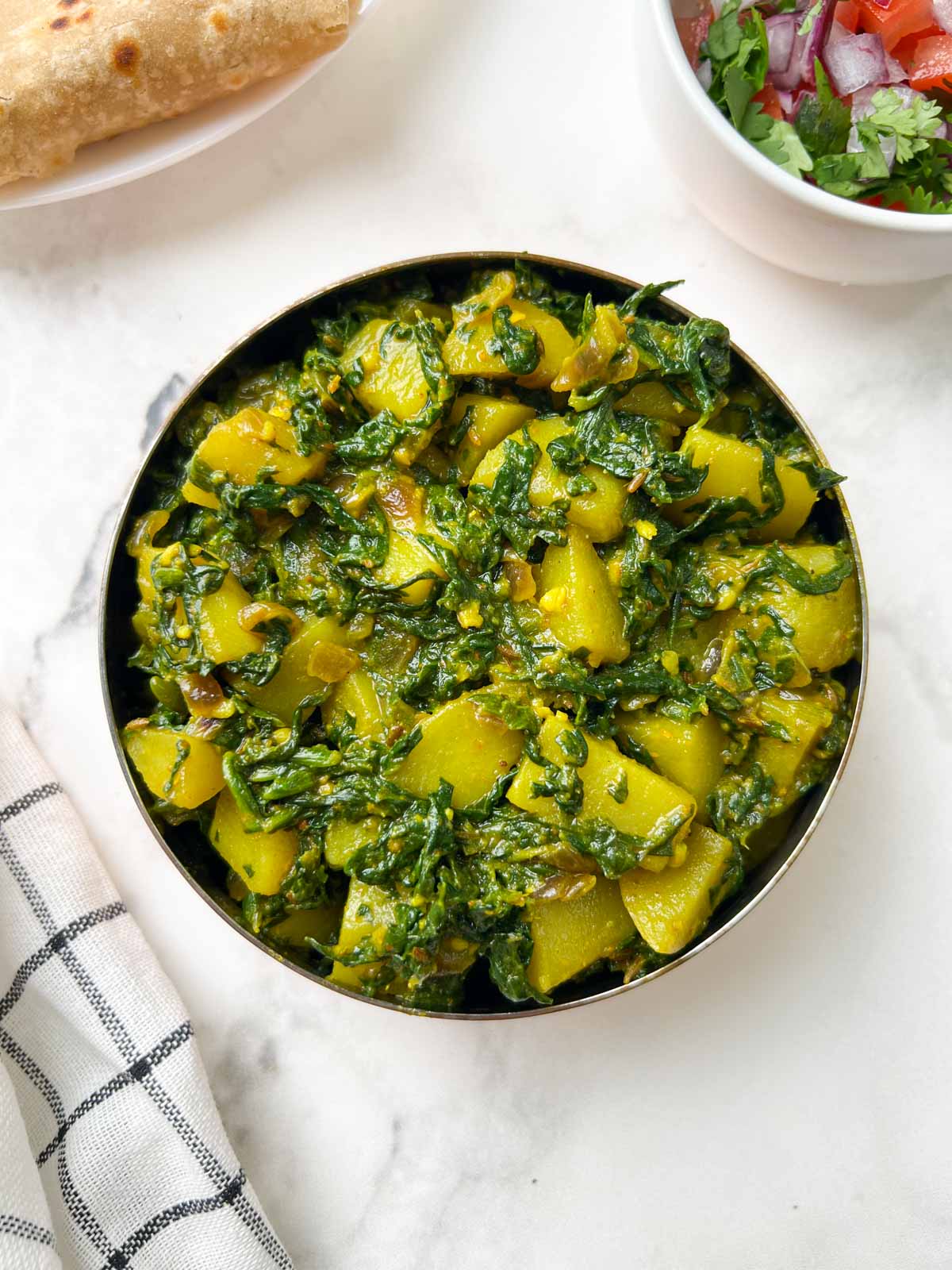 aloo palak sabzi recipe served in a bowl with chapati and salad on the side