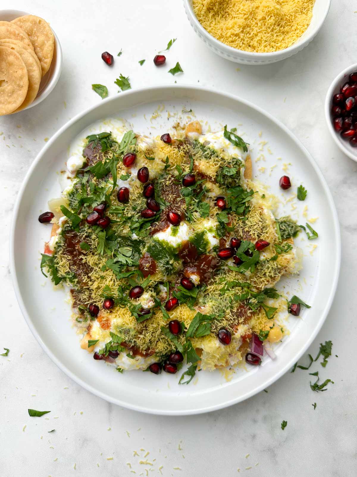 dahi papdi served in a white plate garnished with sev and papdi, dev and chutneys on the side