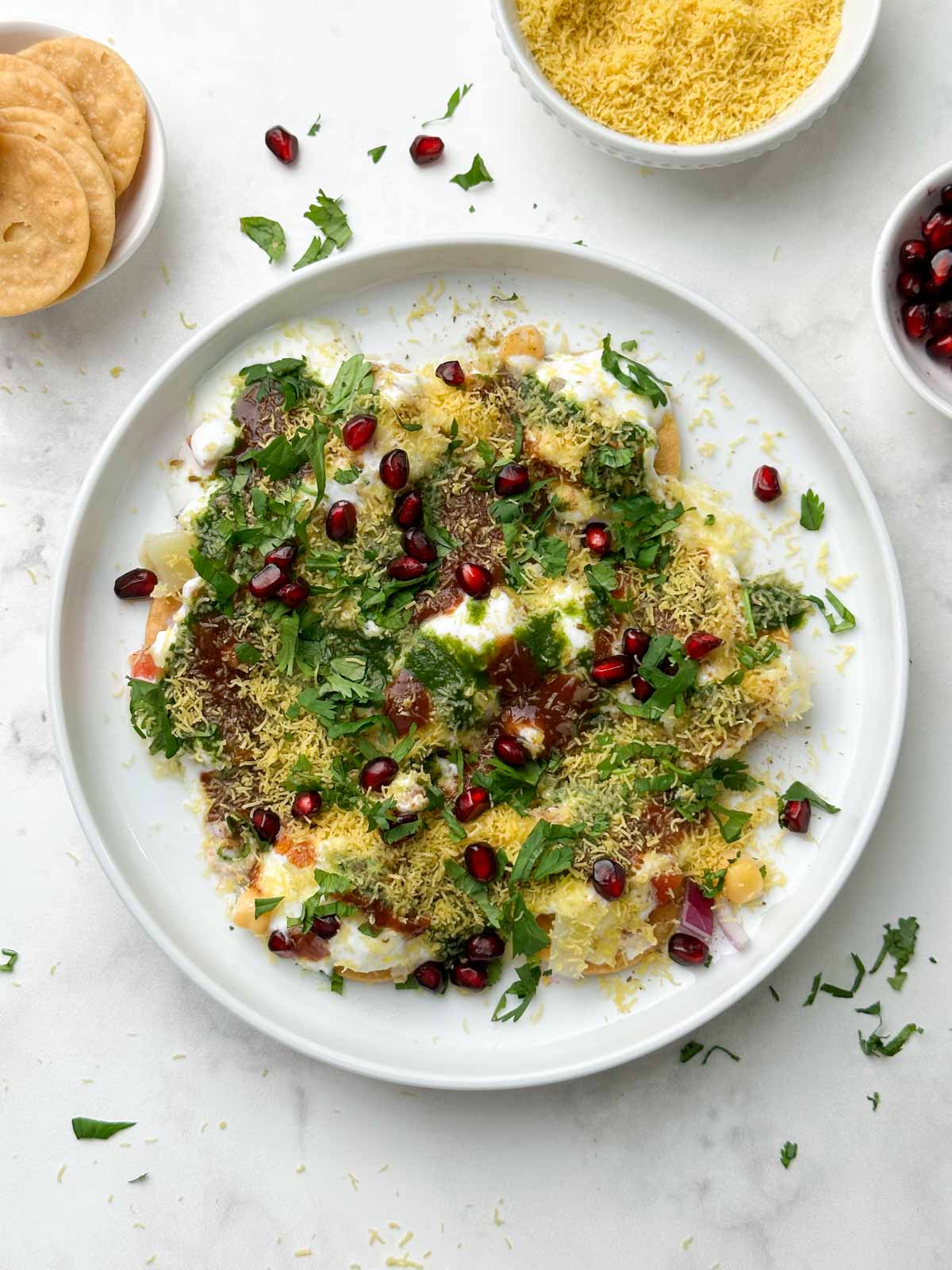 dahi papdi served in a white plate garnished with sev and papdi, dev and chutneys on the side