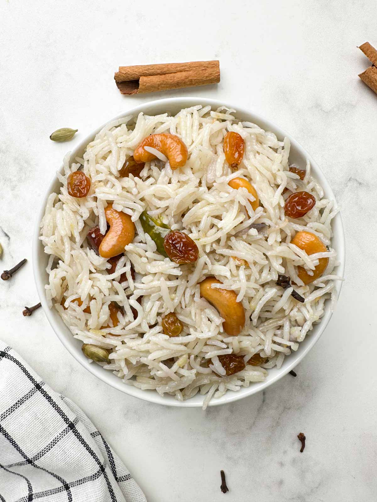 instant pot ghee rice served in a white bowl garnished with nuts and spices on the side