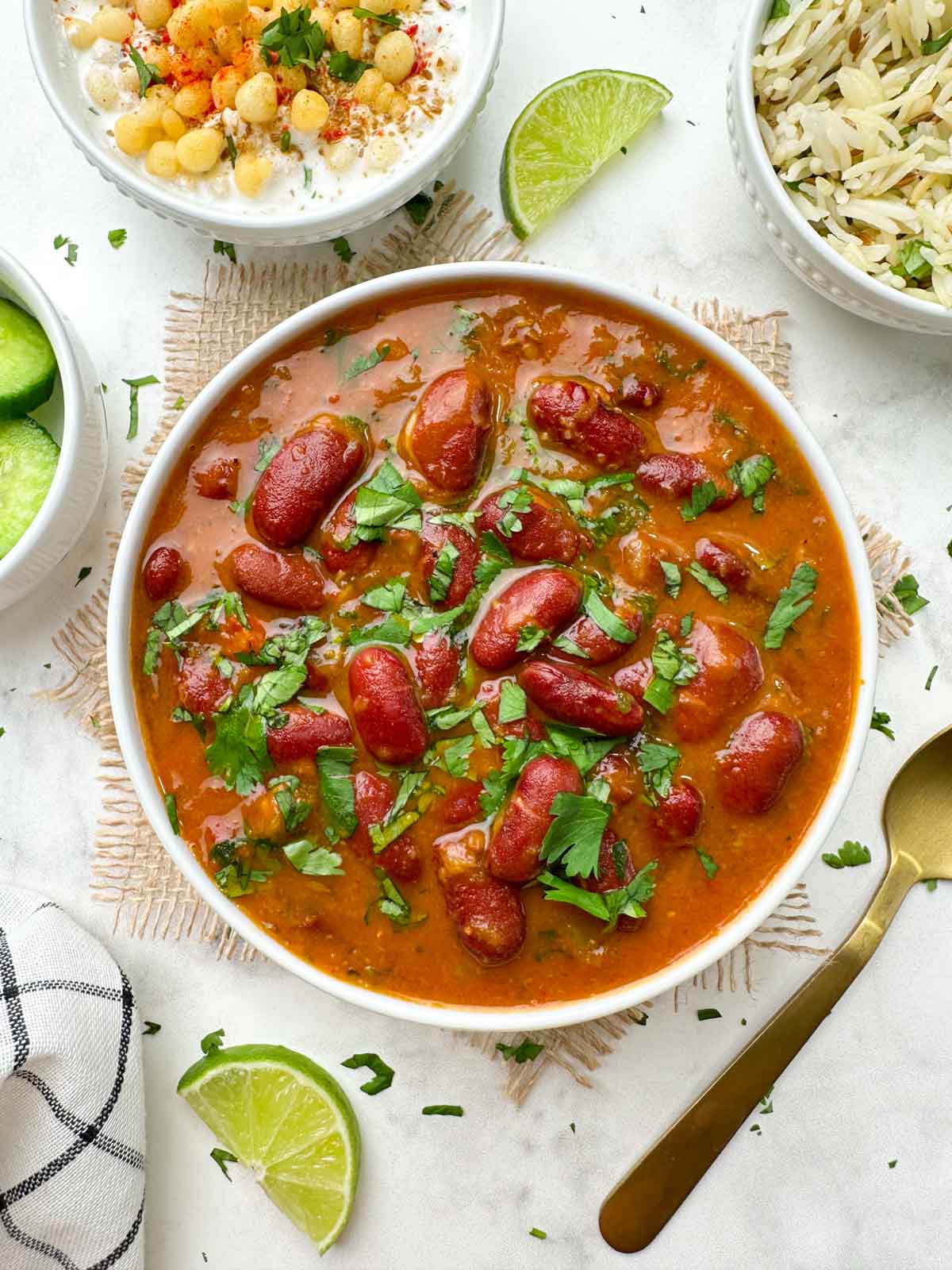 instant pot rajma masala curry served in a bowl garnished with coriander leaves with boondi raita and jeera rice on the side with a lime wedge