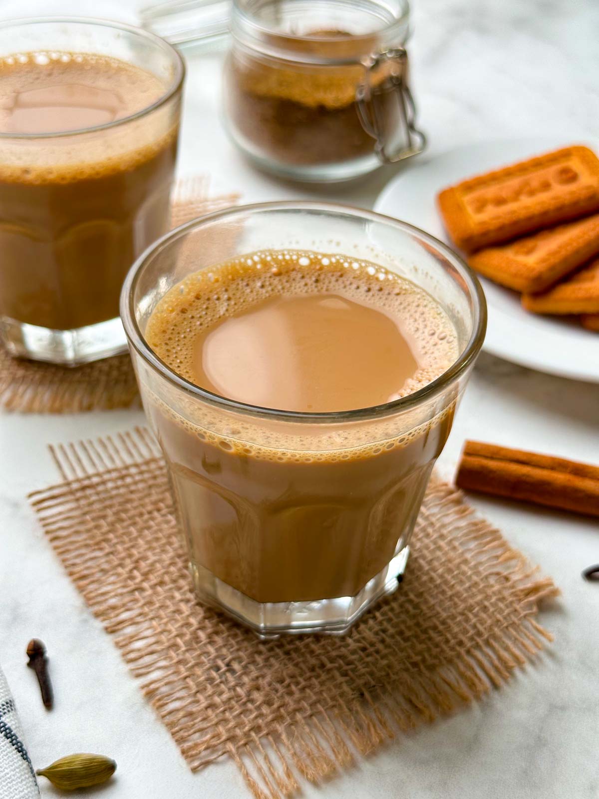 indian masala tea served in a cutting chai glass with biscuits on the side and whole spices around 