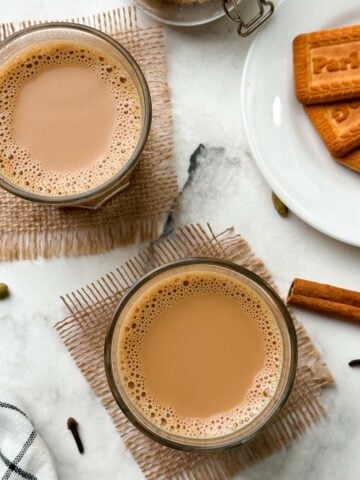 authentic indian masala chai (tea) served in 2 cups with biscuits and chai masala in a mason jar