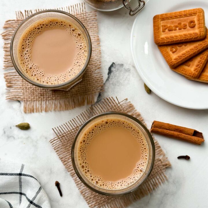 authentic indian masala chai (tea) served in 2 cups with biscuits and chai masala in a mason jar