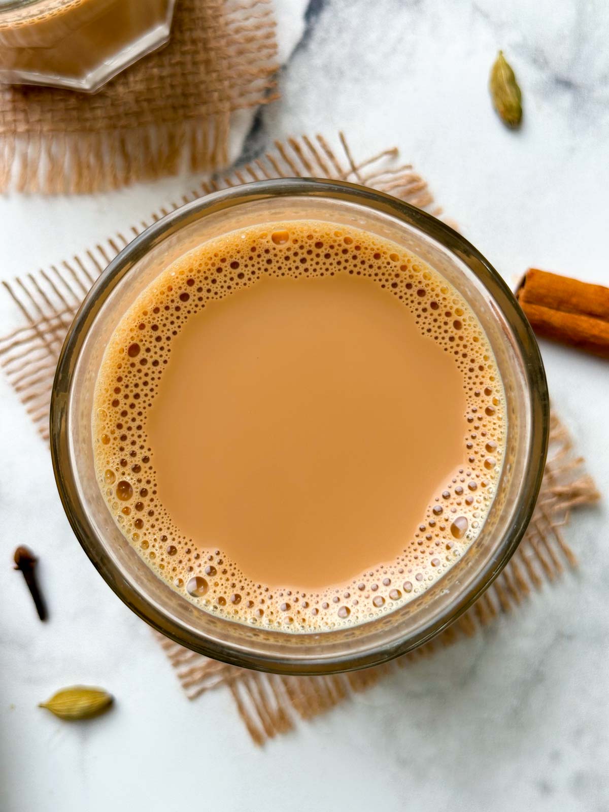 indian masala chai served in a glass cup with whole spices on the side