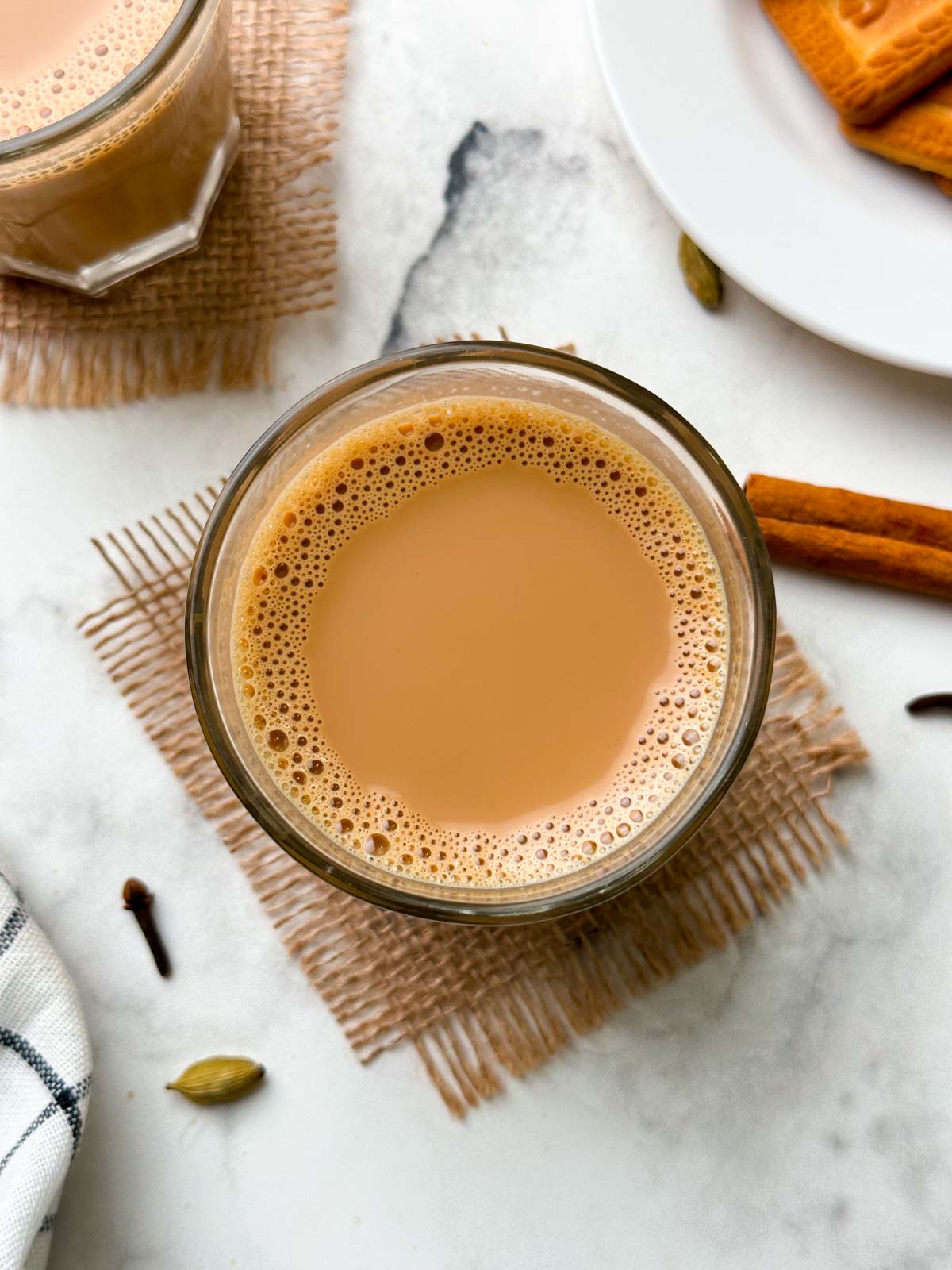 indian masala chai served in a glass cup with whole spices on the side