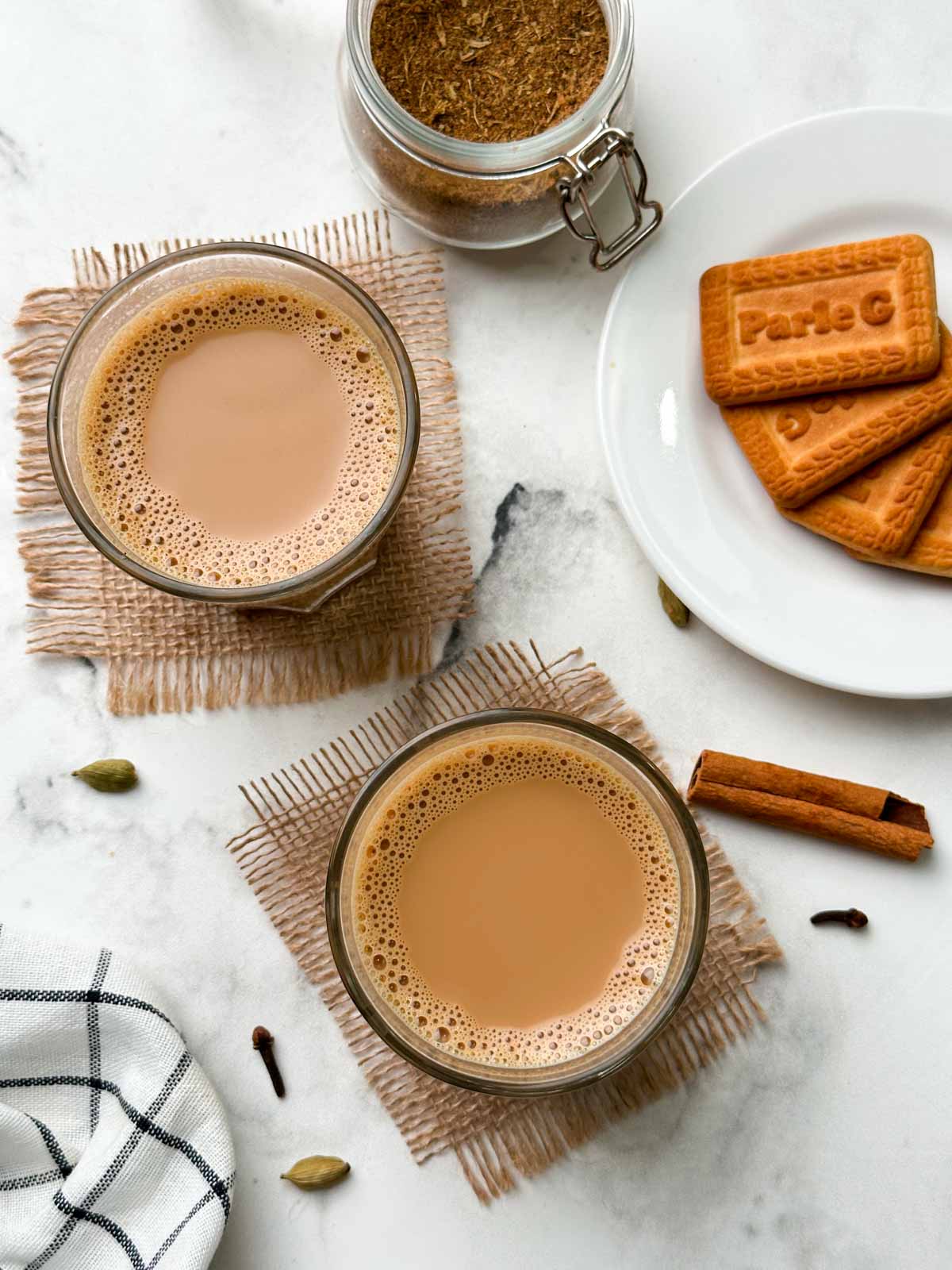 authentic indian masala chai (tea) served in 2 cups with biscuits and chai masala in a mason jar
