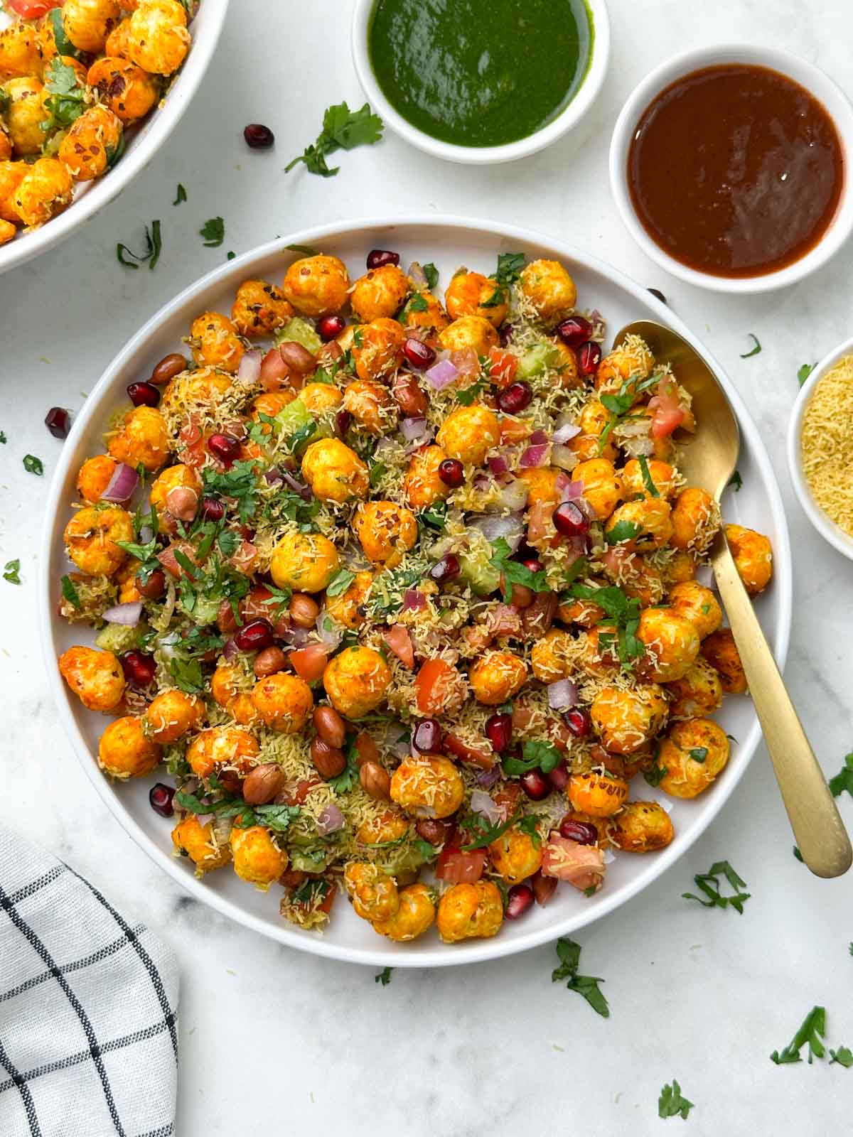 phool makhana bhel served in a plate garnished with sev and pomegranate with a golden spoon and chutneys on the side