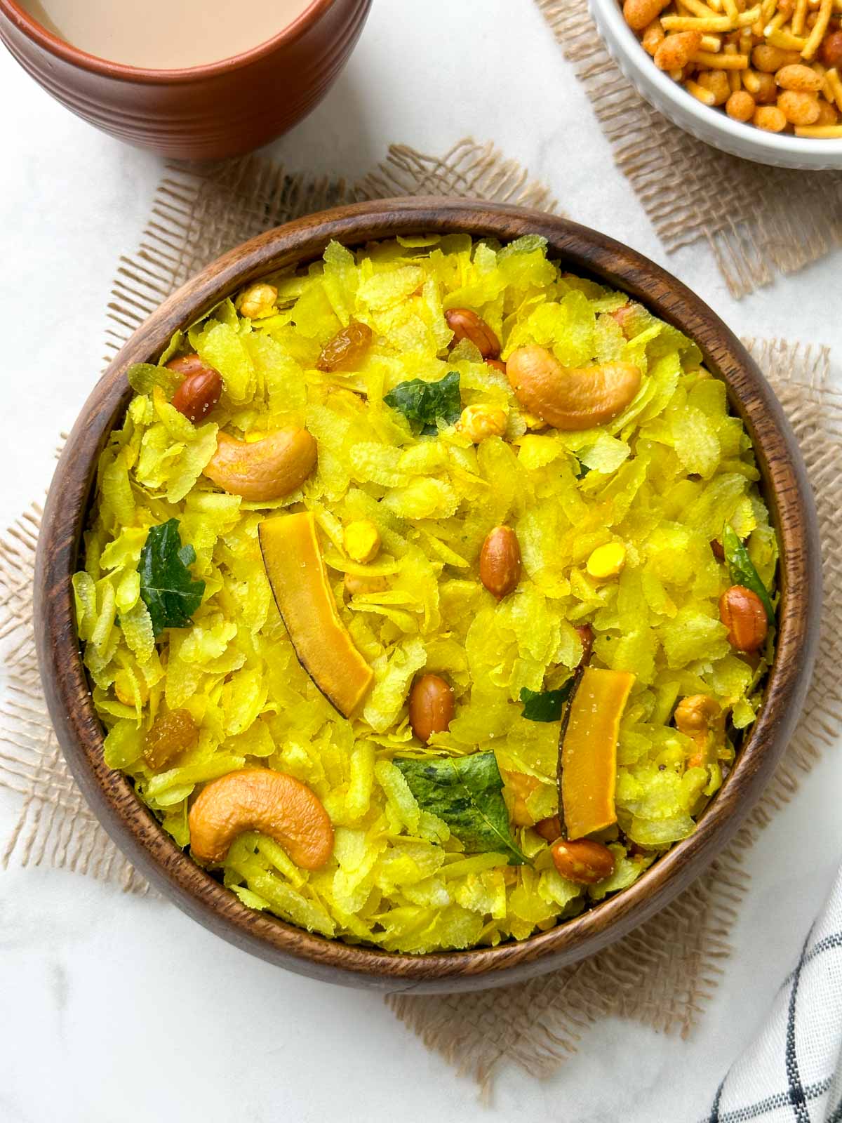 roasted poha chivda (indian namkeen) served in a wooden bowl with sev and masala tea on the side