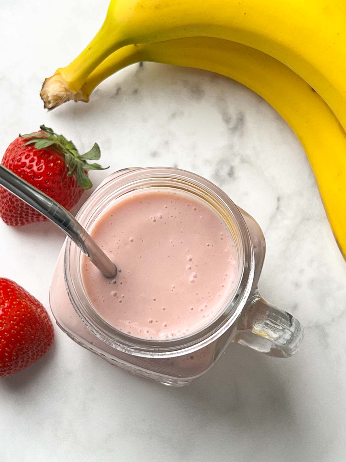 strawberry banana shake served in a mason jar with a steel straw with fruits on the side