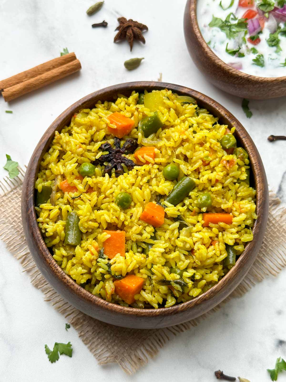 seeraga samba rice biryani in a wooden bowl with raita and whole spices in the side