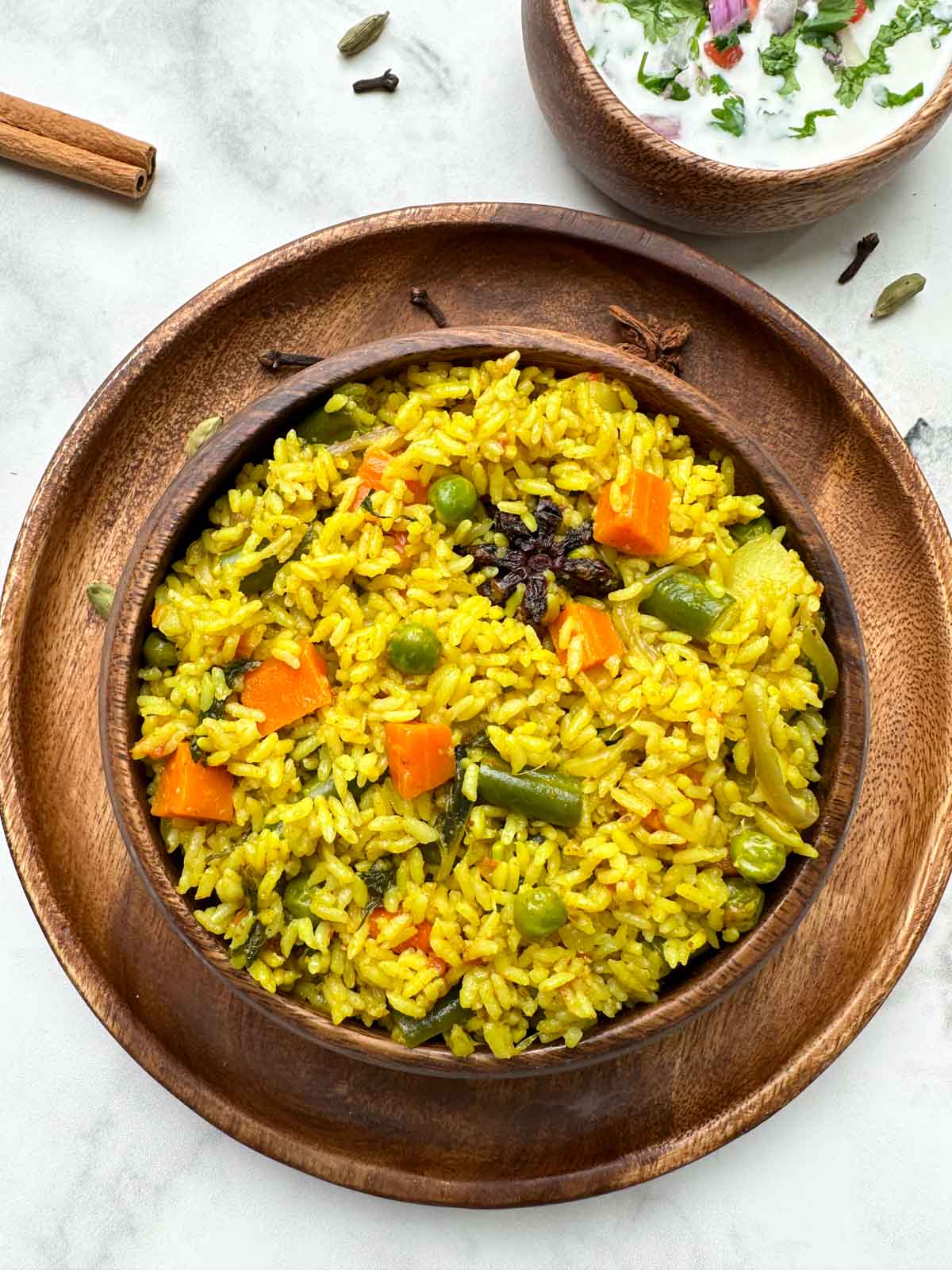 Tamil Nadu style seeraga samba rice vegetable biryani in a wooden bowl with raita and whole spices in the side