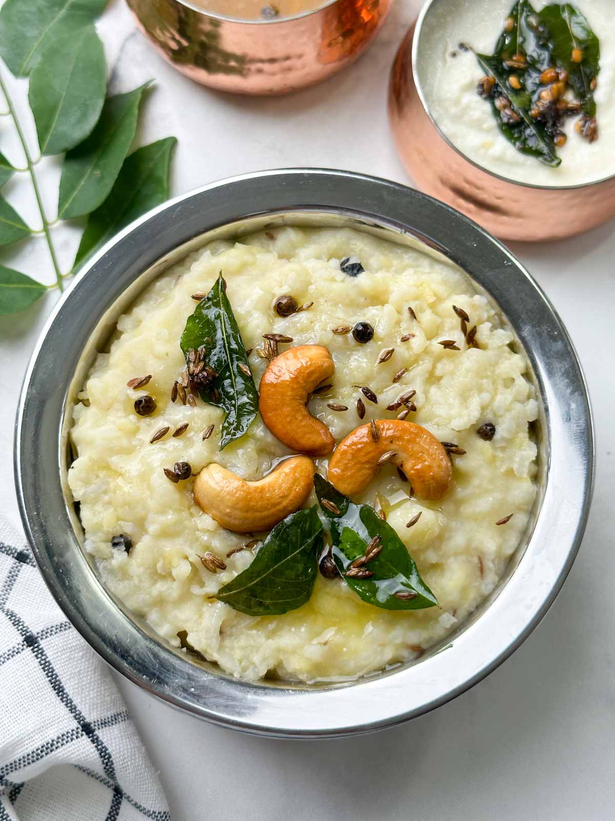 instant pot ven pongal served in a steel bowl garnished with roasted cashews and tempering with coconut chutney and sambar on the side