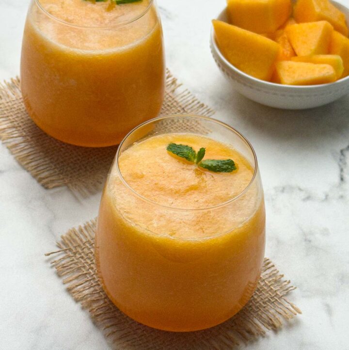cantaloupe (muskmelon) juice served in 2 serving glasses with mint on the top and a bowl of cut cantaloupe pieces
