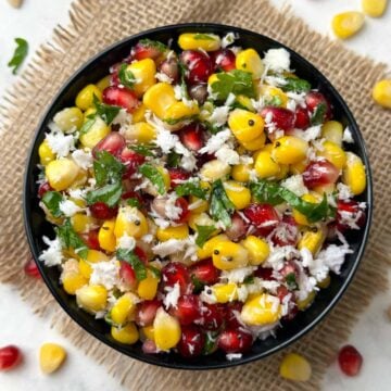 sweet corn pomegranate kosambari served in a black bowl garnished with coriander leaves with corn and pomegranate on the side
