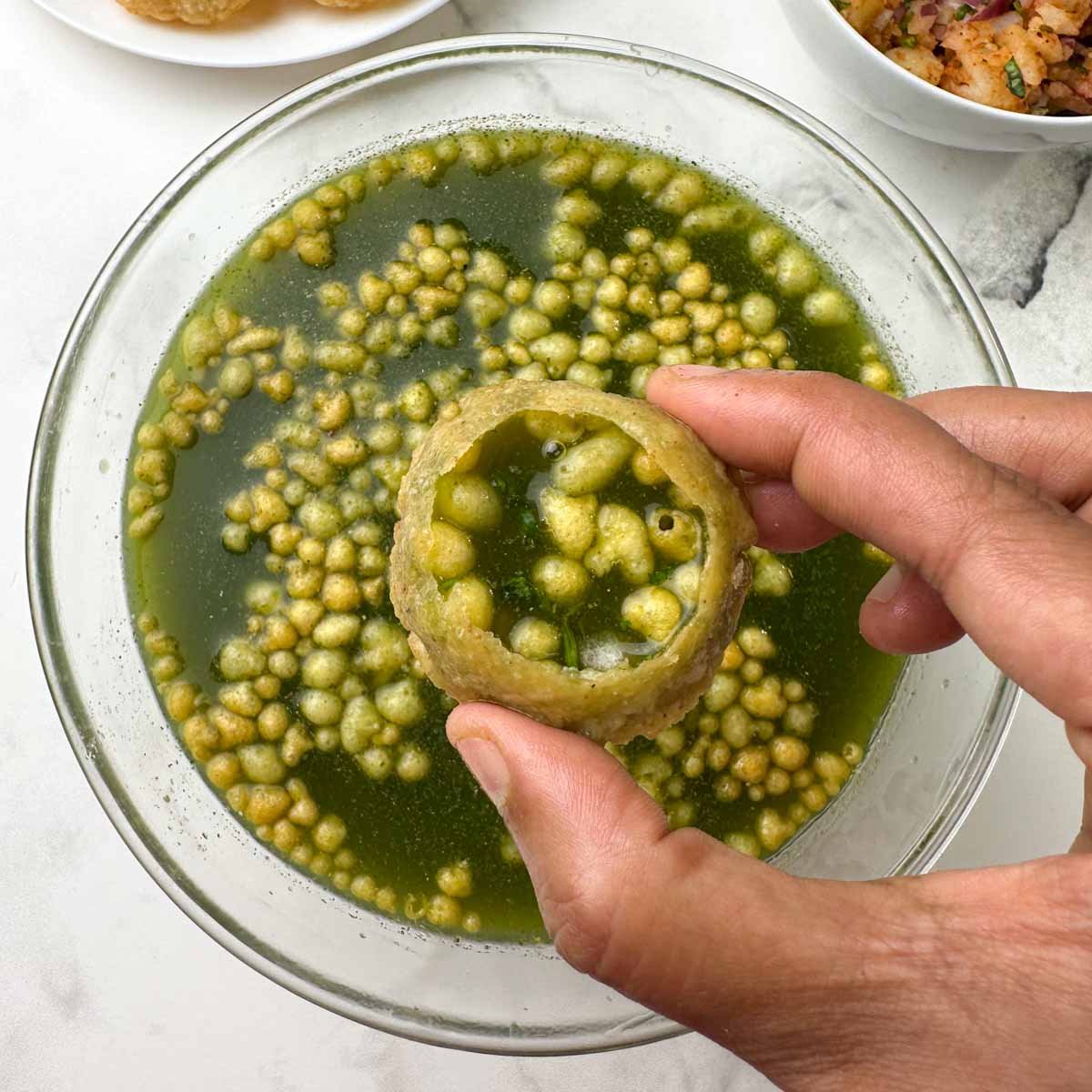 pani puri (golgappa) in hand with puri and potato mixture on the side