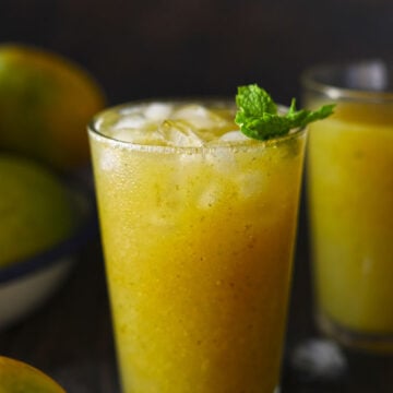 Aam panna served in two glasses garnished with mint leaves and mangoes on the side.