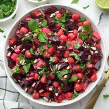 beetroot chickpea salad served in a bowl garnished with sunflower seeds and cucumber, coriander on the side