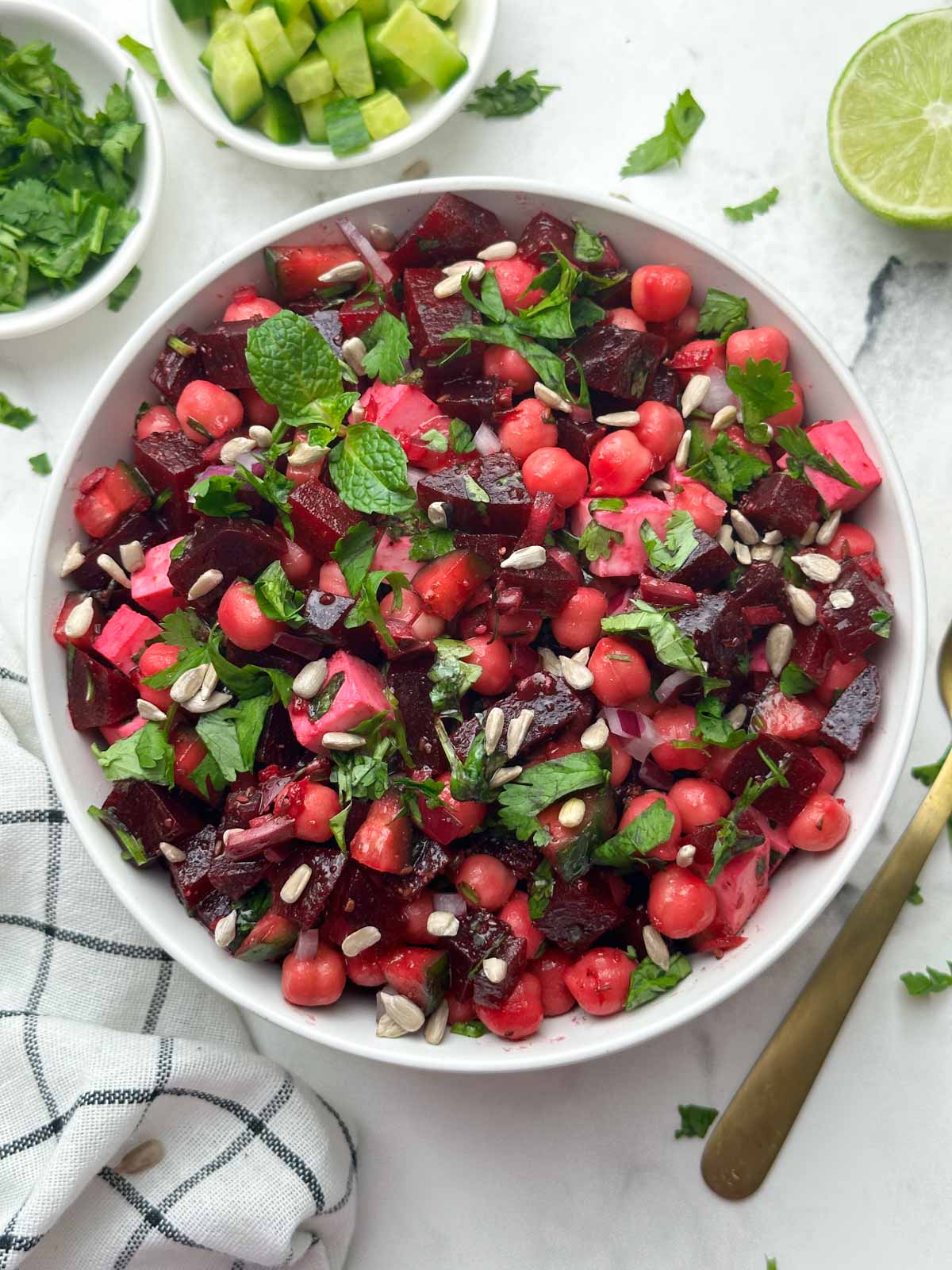 beet chickpea salad served in a bowl garnished with sunflower seeds and cucumber, coriander on the side