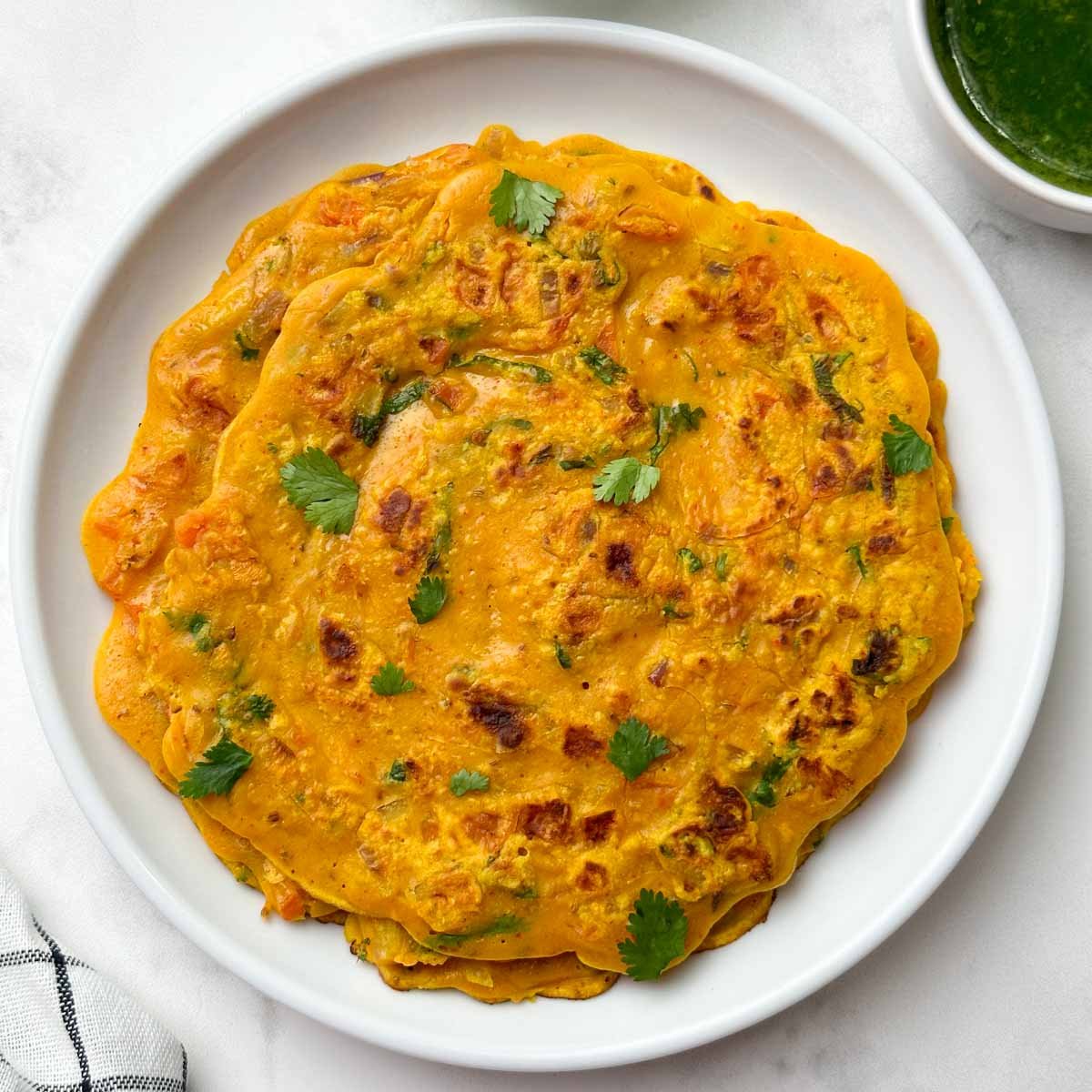 Besan chilla served on a plate with green chutney on the side.