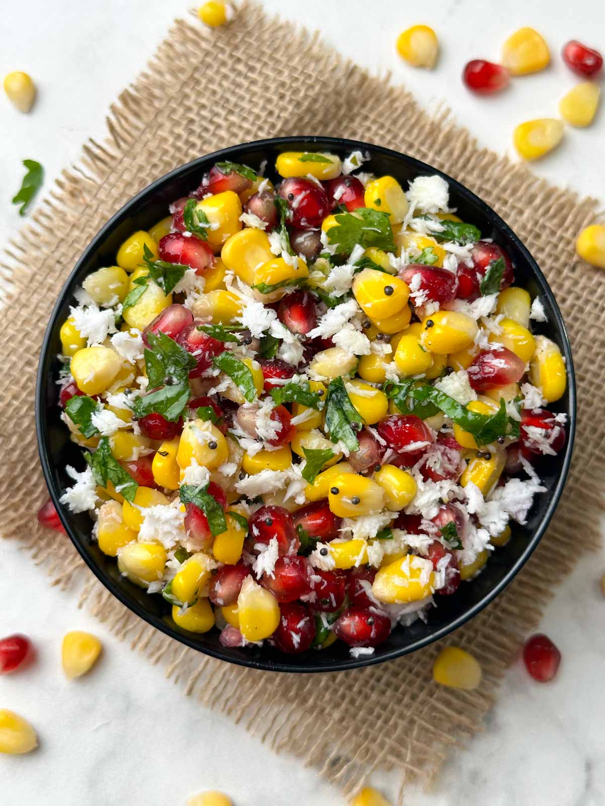 sweet corn pomegranate kosambari (salad) served in a black bowl garnished with coriander leaves with corn and pomegranate on the side