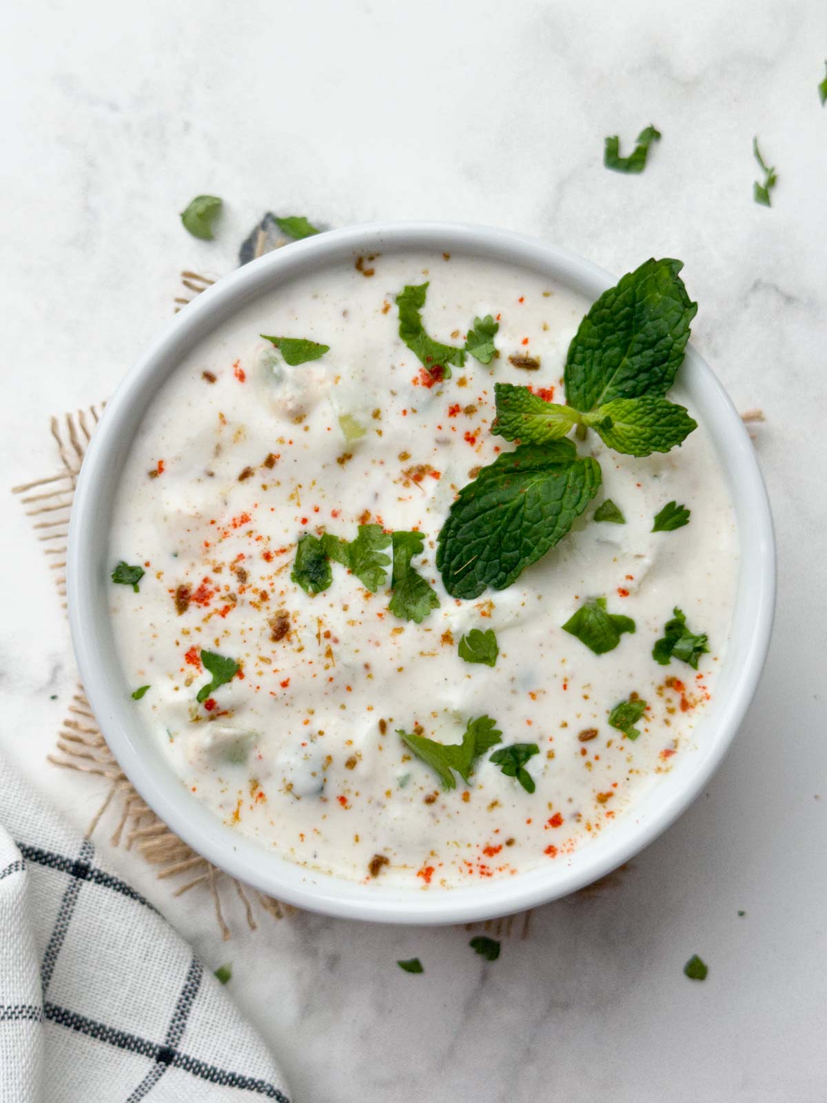 cucumber raita served in a bowl garnished with coriander and mint leaves