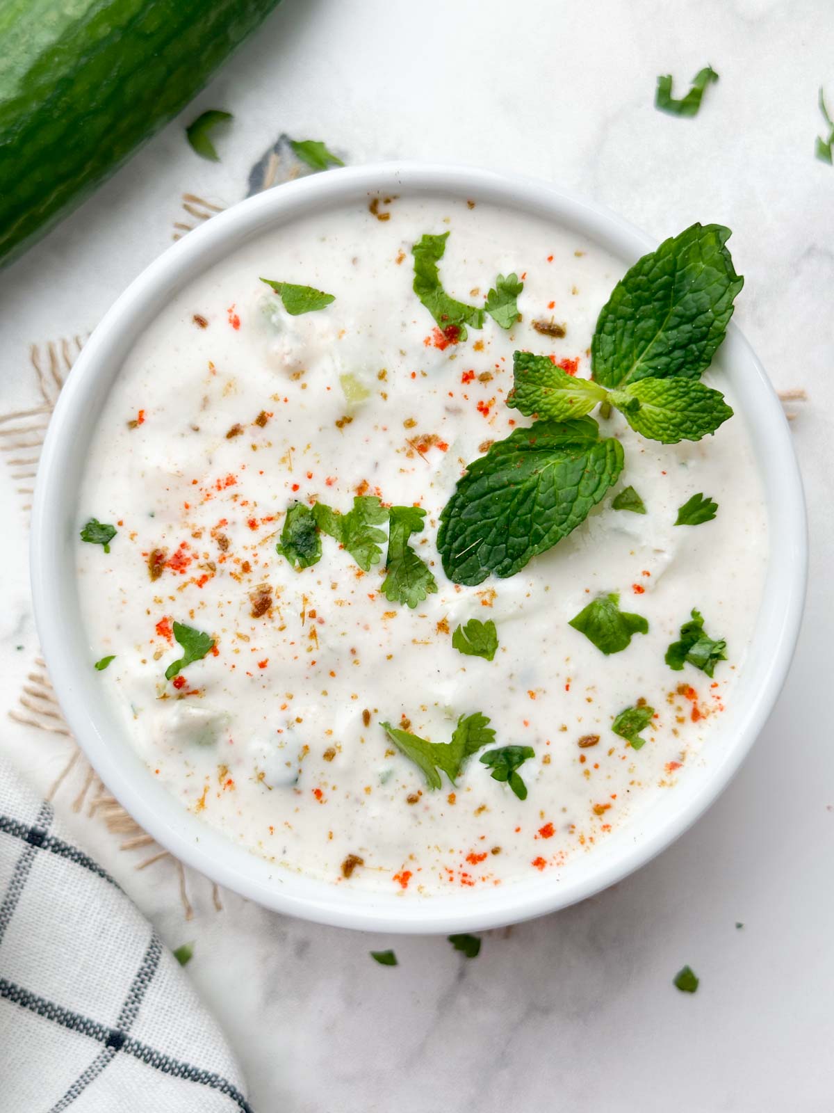 cucumber raita served in a bowl garnished with coriander and mint leaves