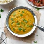 restaurant style dal fry served in a bowl garnished with coriander leaves with a steel spoon and rice and onion salad on the side