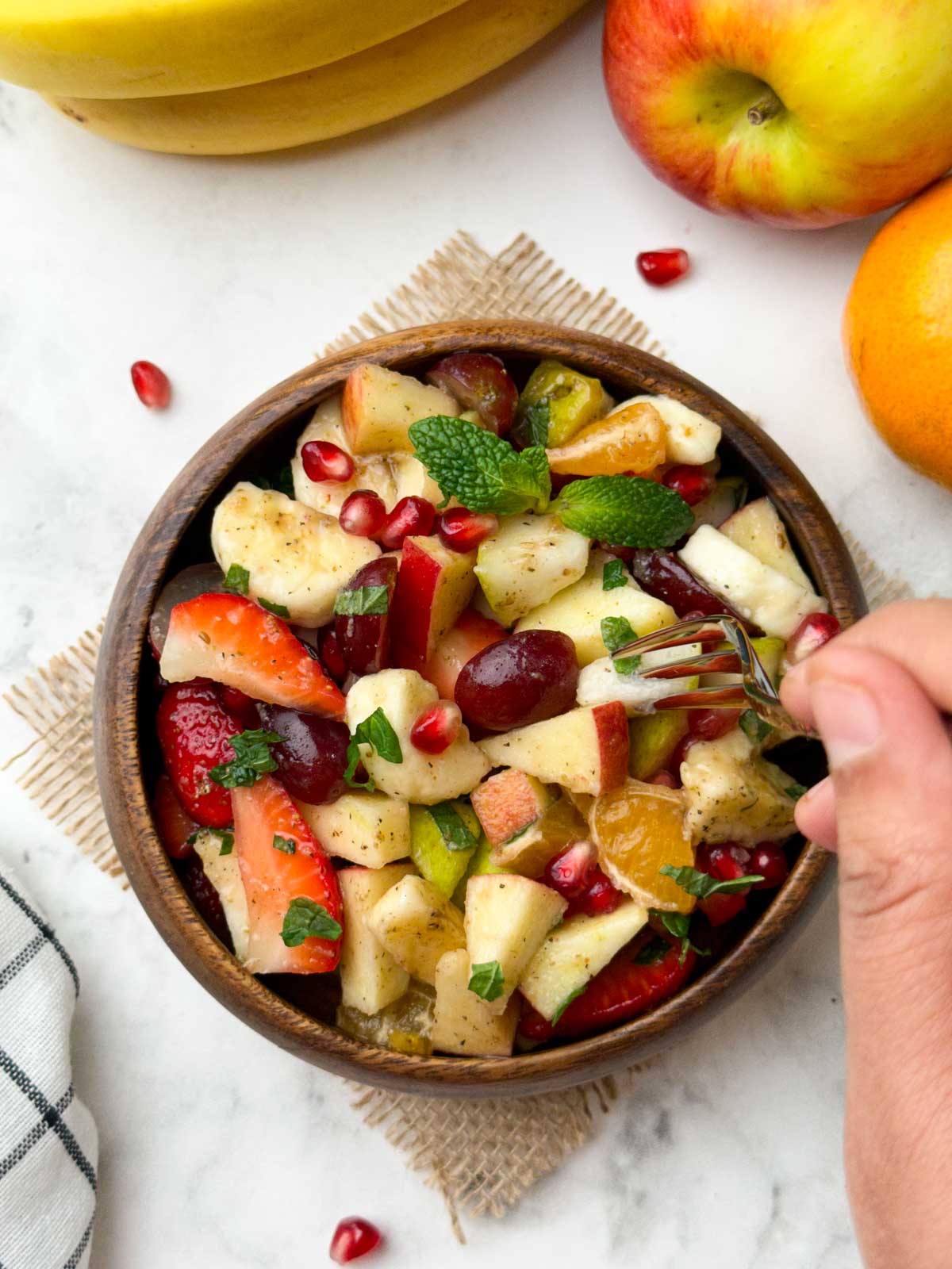 fruit chaat served in a wooden bowl with fork and fruits on the side