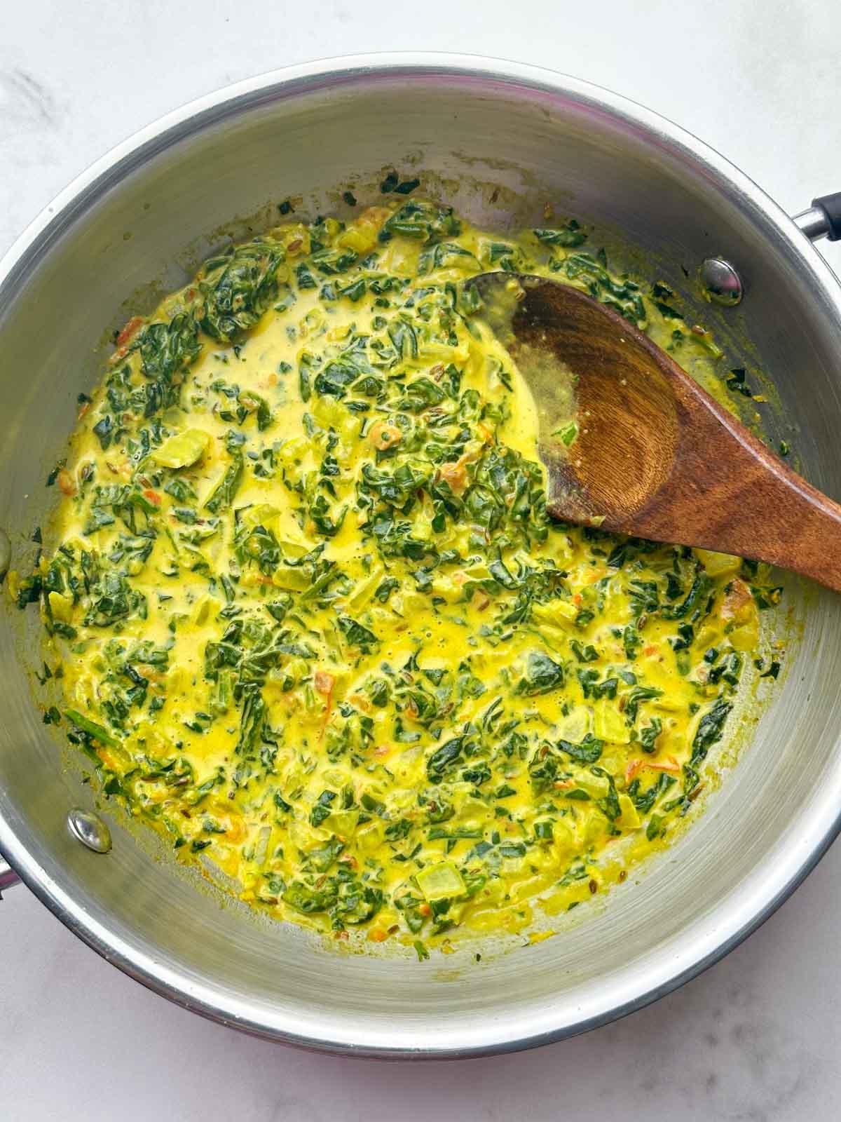 Indian creamed spinach in a kadai with wooden spoon on the top