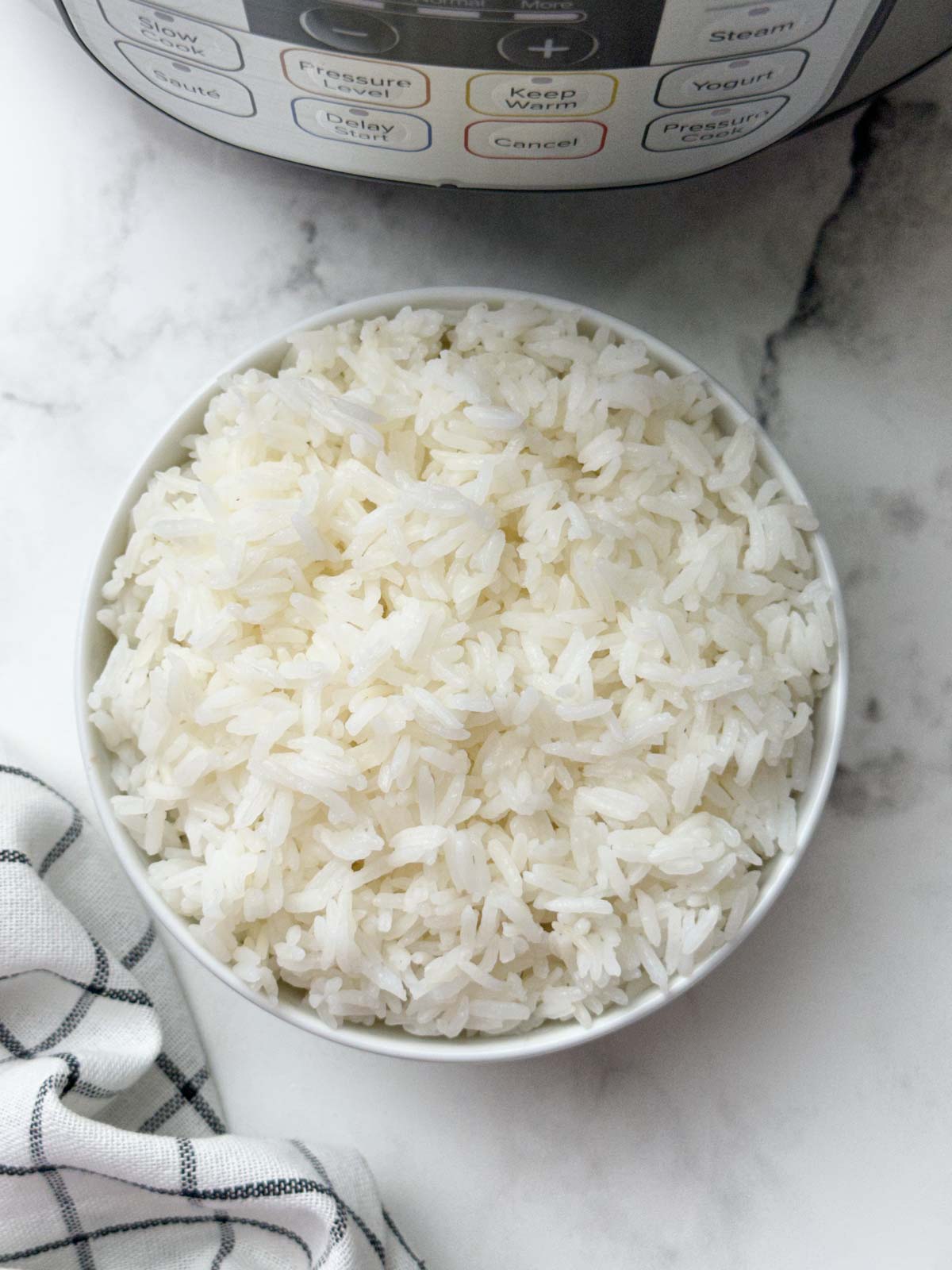 Jasmine rice in a white bowl and instant pot and napkin on the side 