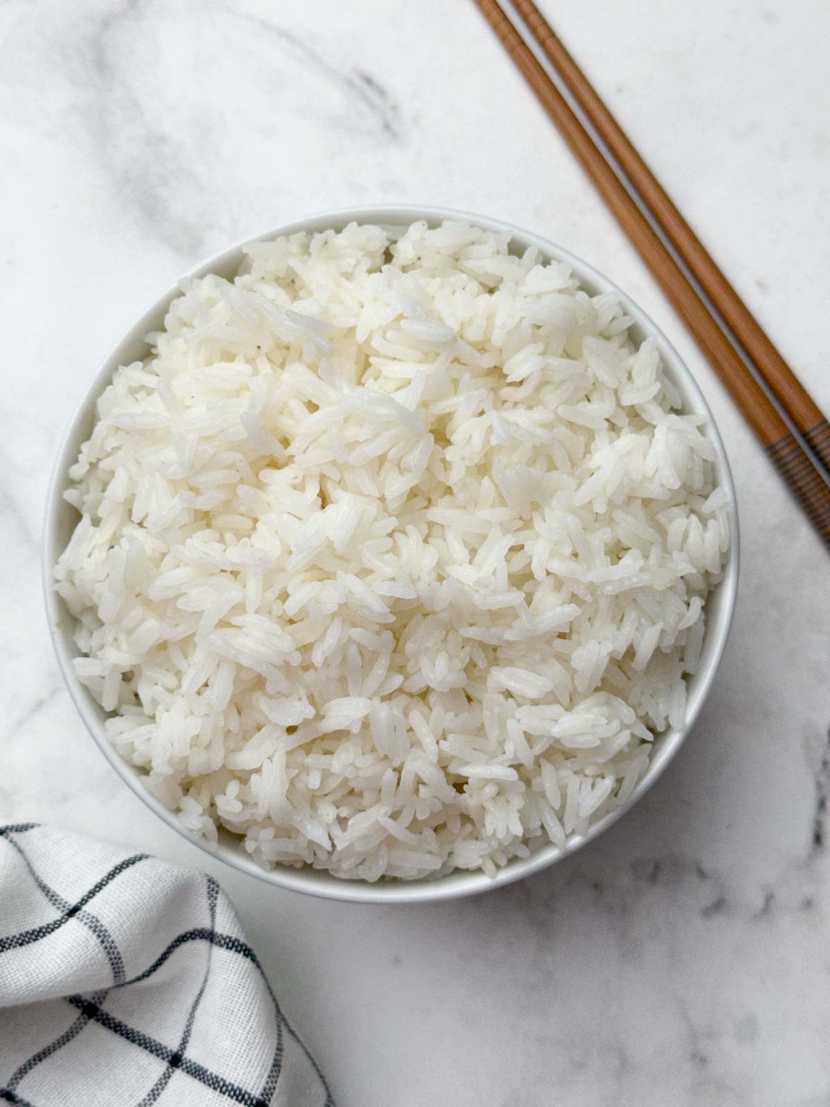 jasmine rice in a white serving bowl with chopsticks on the side