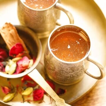 Kashmiri kahwa served in silver mug with cardamom and dried rose petals on the side.