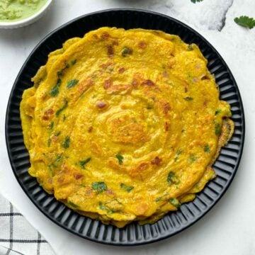 moong dal chilla stacked on a plate with pickle and coconut chutney on the side