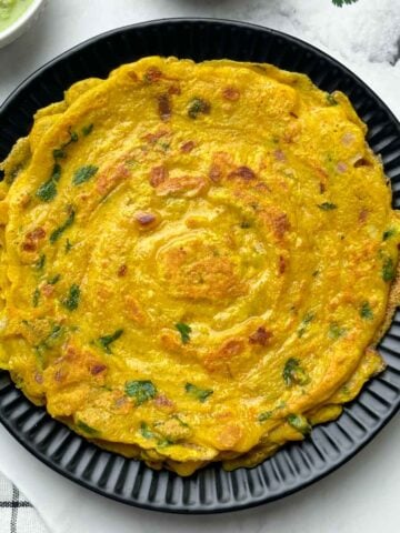 moong dal chilla stacked on a plate with pickle and coconut chutney on the side