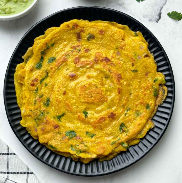 moong dal chilla stacked on a plate with pickle and coconut chutney on the side