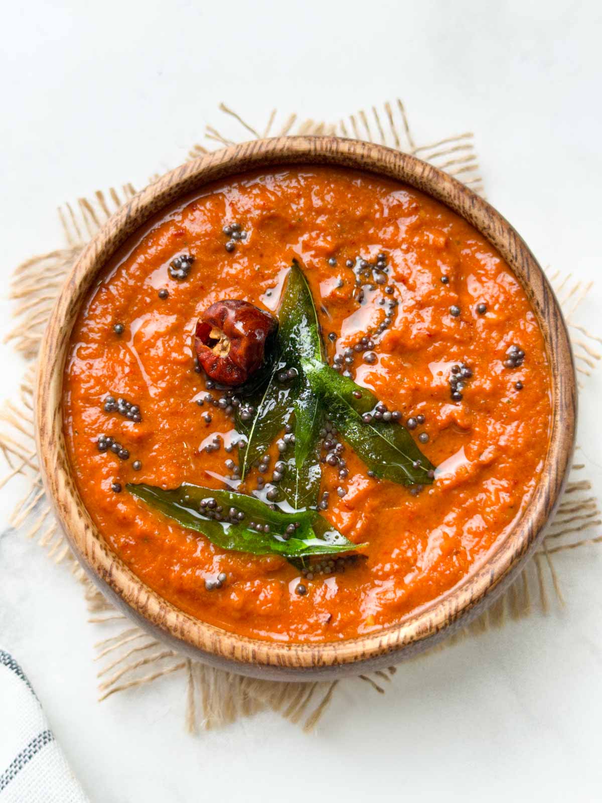 onion chutney served in a wooden bowl with tempering on the top and whole red onion on the side