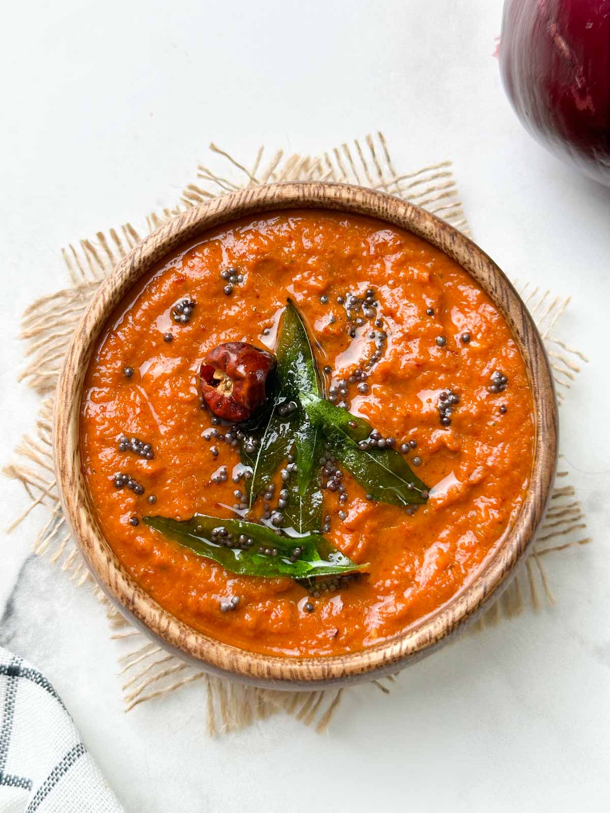 onion chutney served in a wooden bowl with tempering on the top and whole red onion on the side