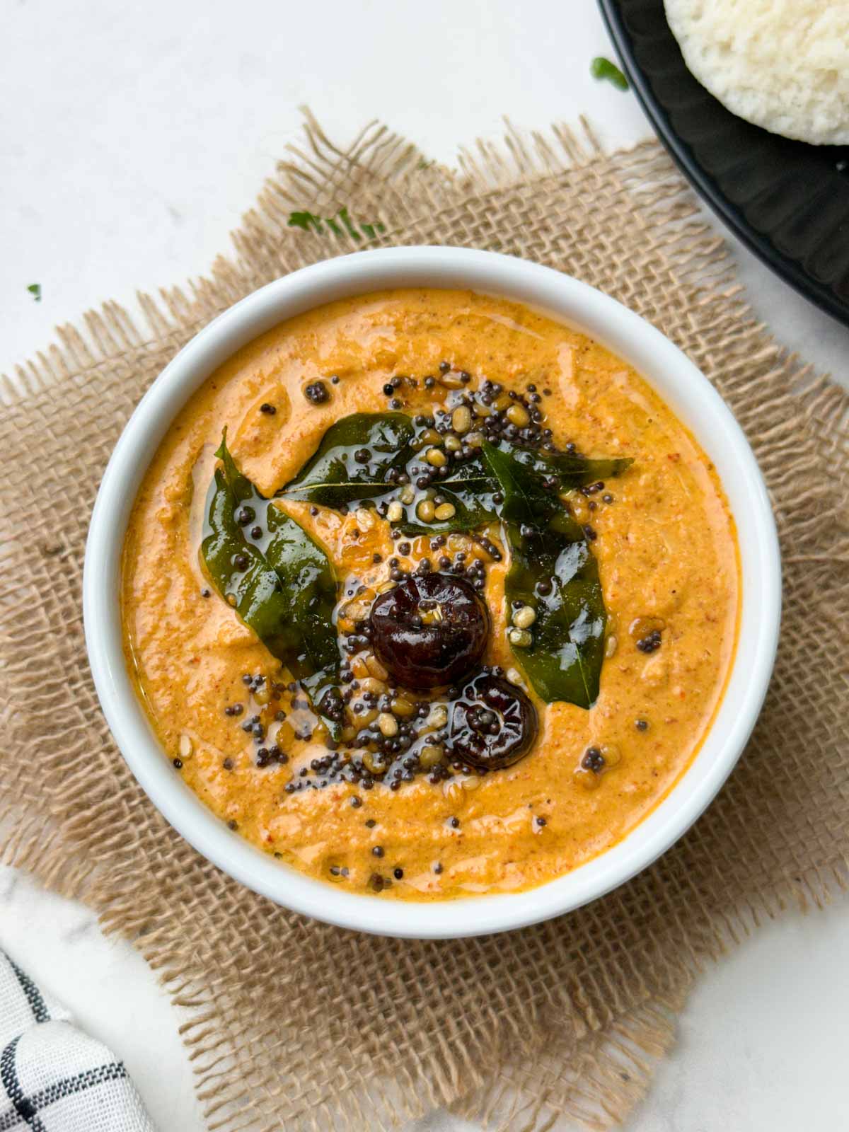 peanut chutney recipe served in a bowl with tempering on the top with idli on the side.
