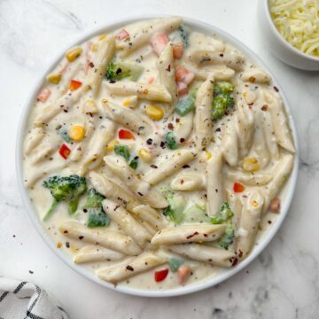 white sauce penne pasta (bechamel sauce pasta) served in a plate with cheese on the side