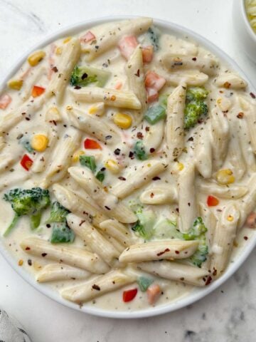 white sauce penne pasta (bechamel sauce pasta) served in a plate with cheese on the side