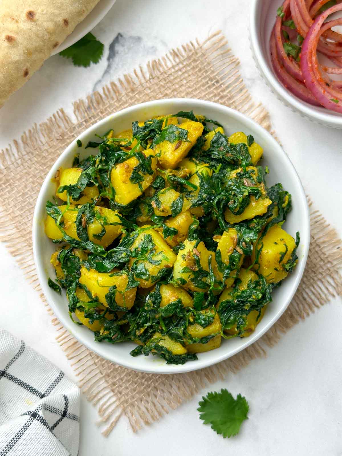 aloo methi sabzi served in a bowl with chapati and onion salad on the side