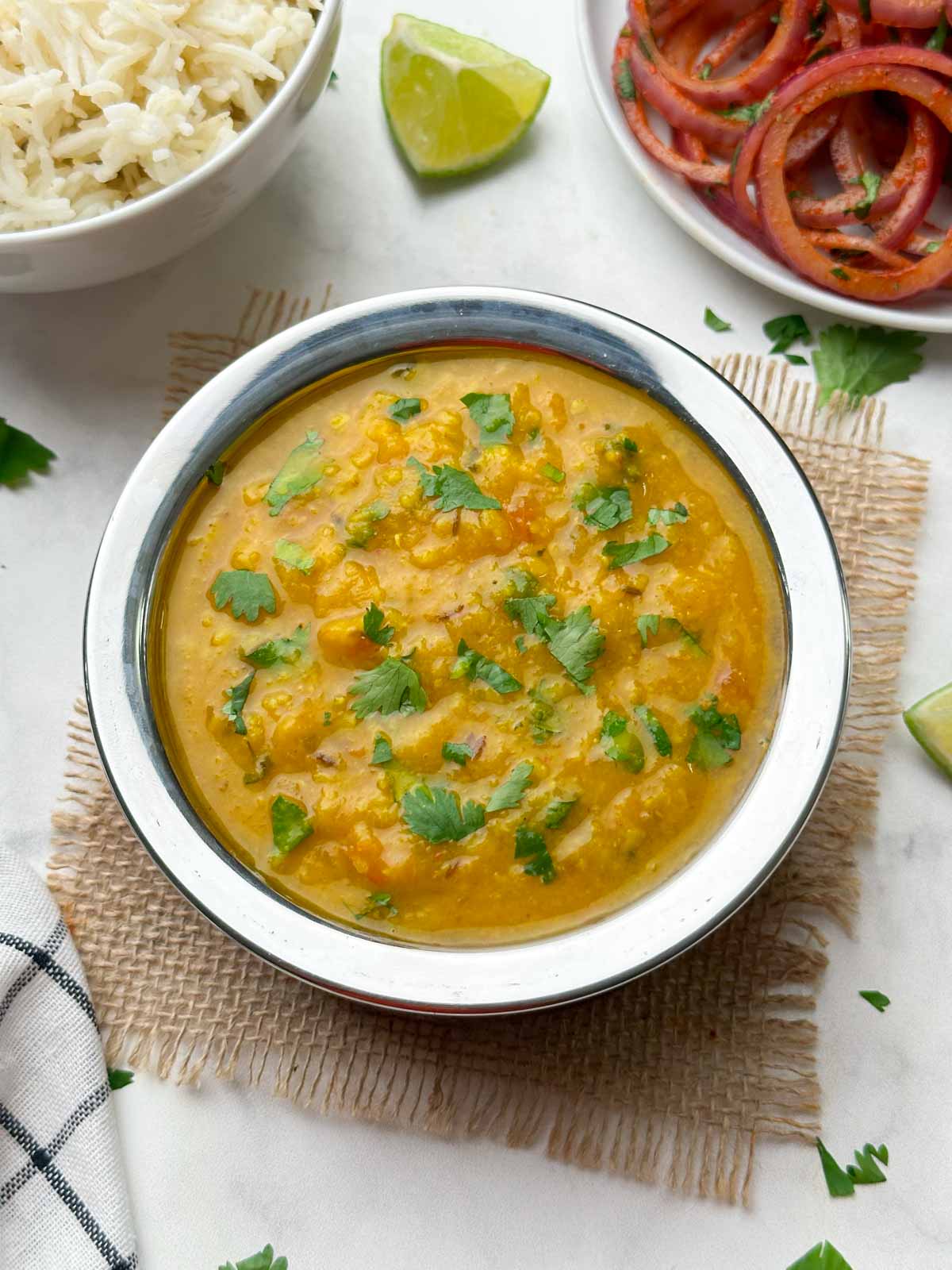 Dal fry served in a bowl garnished with coriander leaves and rice and onion salad on the side