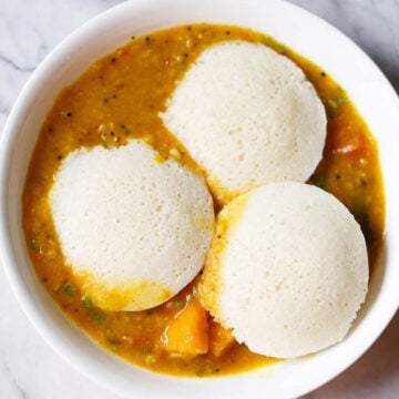 Three idlis in a bowl full of vegetable sambar.