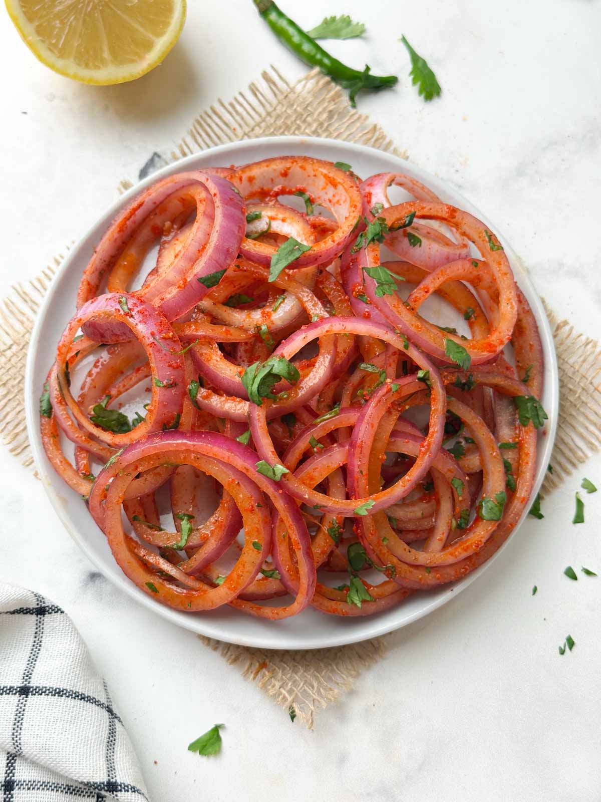 laccha pyaaz (indian onion salad) served on a plate with slice of lemon and green chili on the side