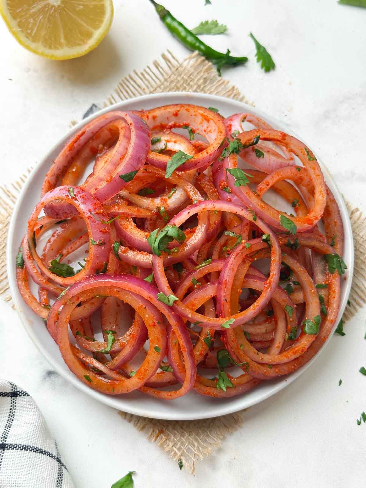 laccha pyaaz (indian onion salad) served on a plate with slice of lemon and green chili on the side
