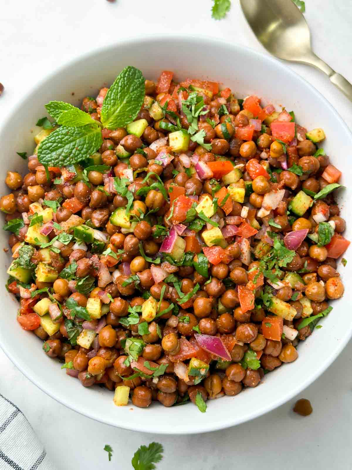 kala chana salad (black chickpeas salad) served in a bowl garnished with mint and spoon on the side