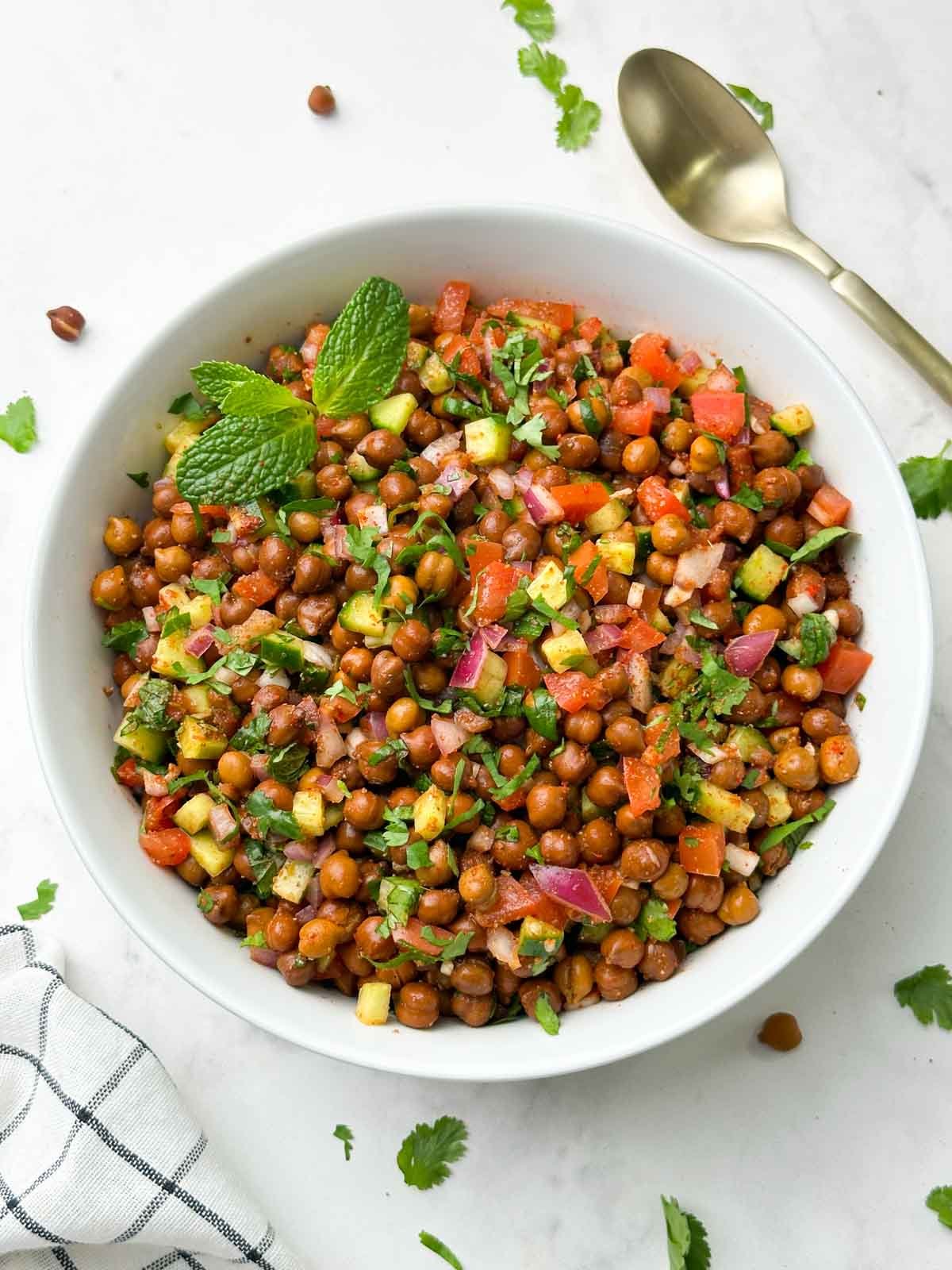 kala chana salad (black chickpeas salad) served in a bowl garnished with mint and spoon on the side